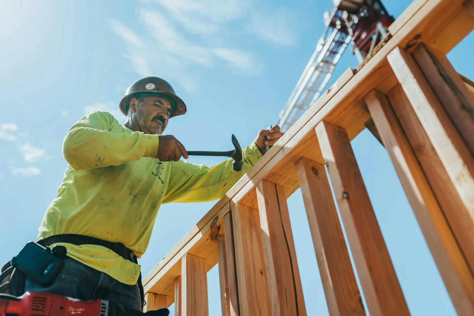 A carpenter nailing the frame of a house addition under a blue sky
