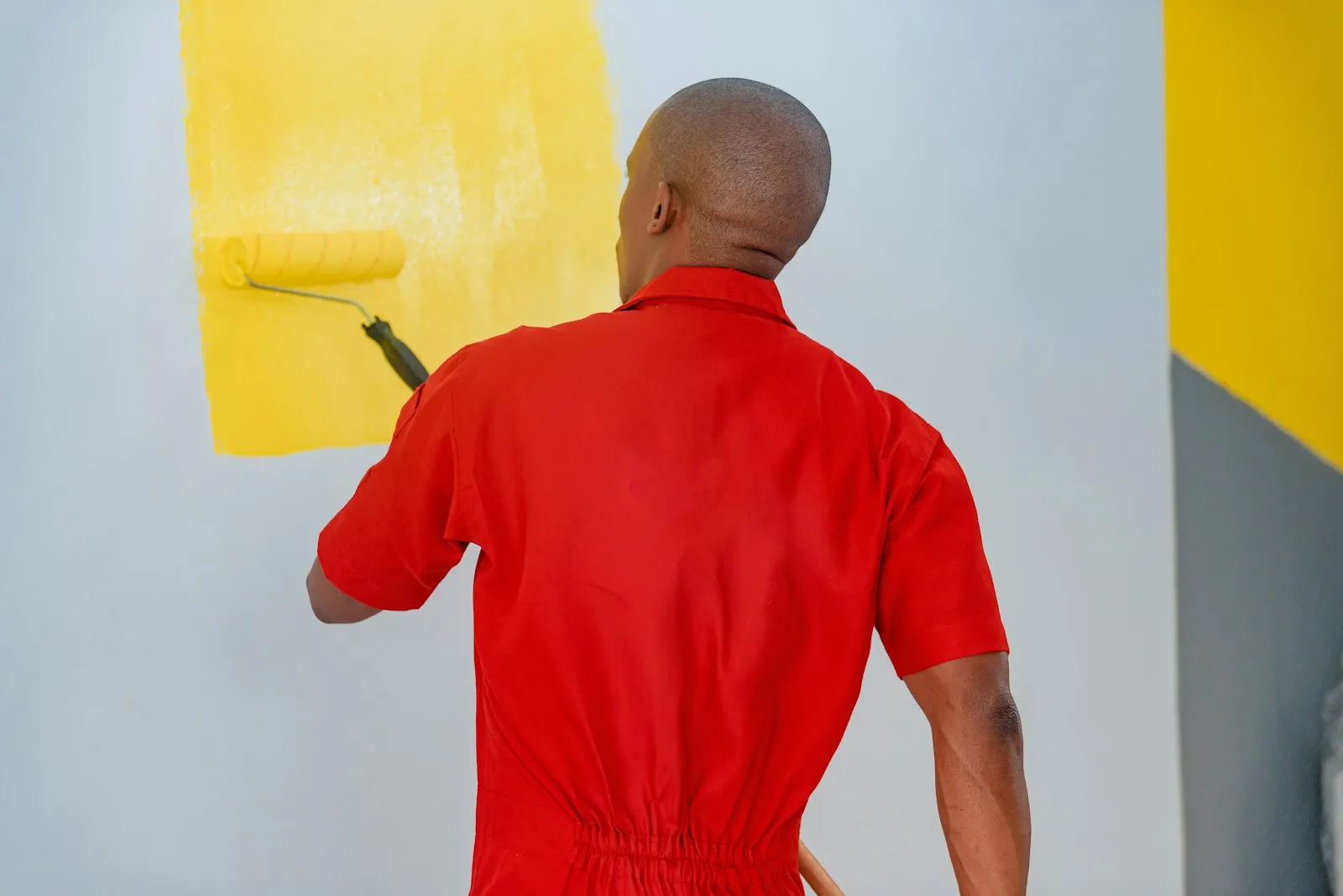 A painter rolling yellow paint onto a white wall