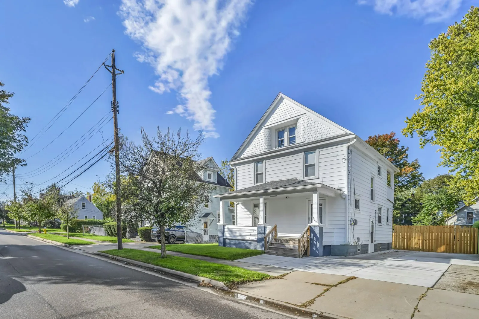 A white two-story house with a front porch on a quiet residential street